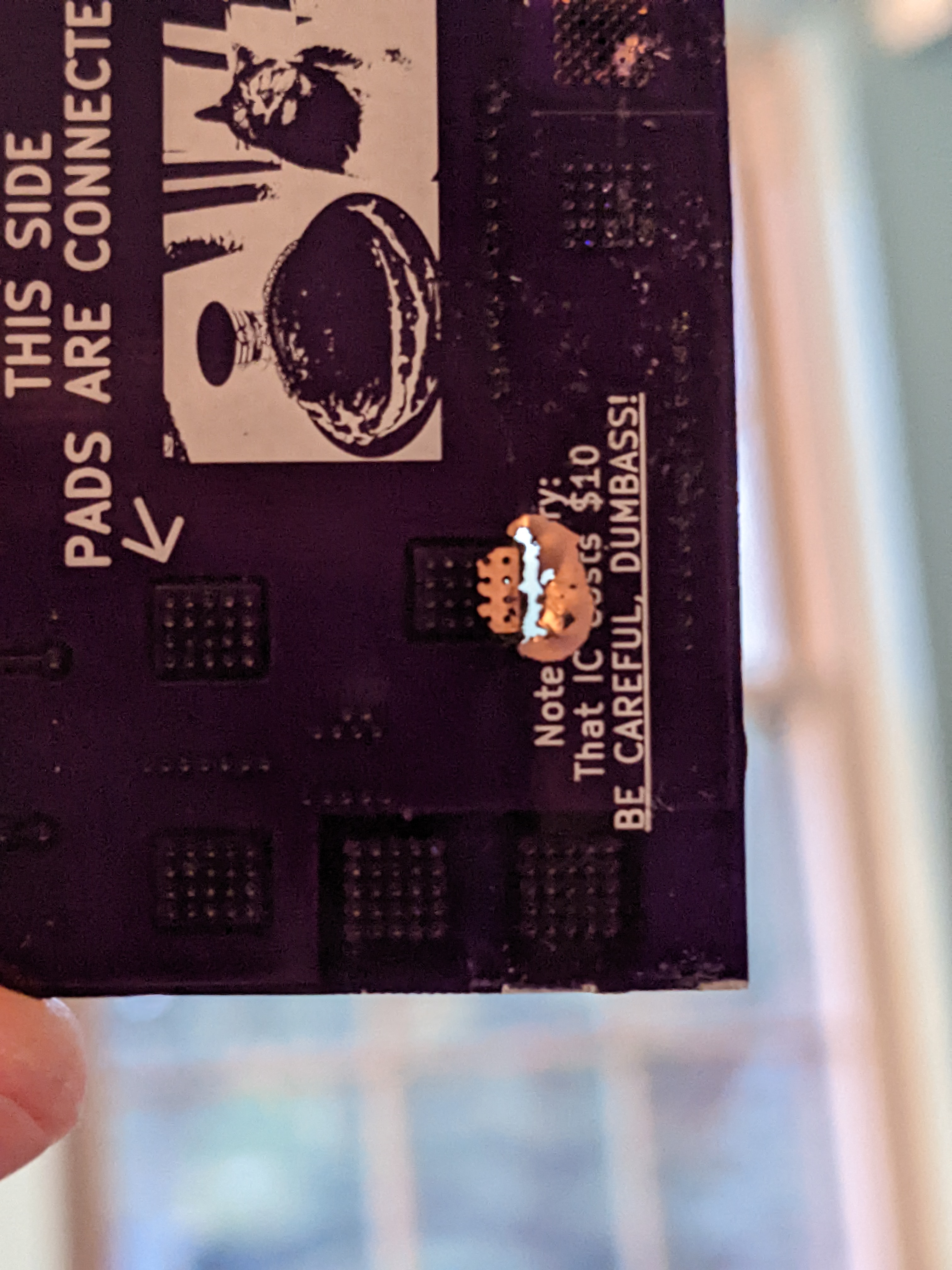 The back of a circuit board showing a pea-sized hole blown through a message on the silkscreen that reads 'be careful, dumbass'